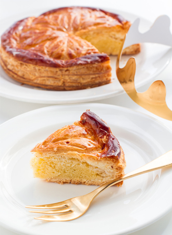 Part généreuse de galette des rois dans une assiette au premier plan et une galette des rois entière en second plan.