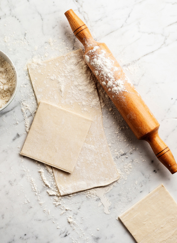 Morceaux de pâte feuilletée avec un rouleau à pâtisserie par-dessus, prêts à être travaillés.