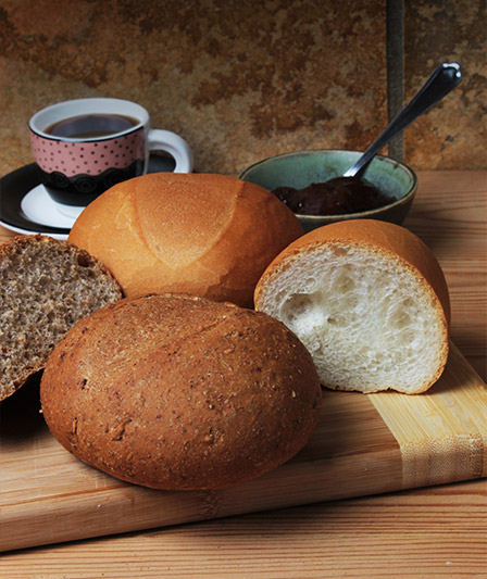Petits pains blancs moelleux et petits pains gris, accompagnés d'un café en arrière-plan.