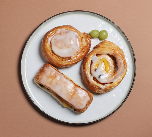 Assiette de viennoiseries avec deux couques suisses rondes et une couque suisse longue, fournies par Panistar, fournisseur de viennoiseries crues surgelées pour les boulangeries.